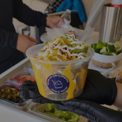 Nachos Cart by Snack Sized Food Cart in Lancaster CA Owner Hannah Serraino holding cup of nachos with sour cream and guacamole